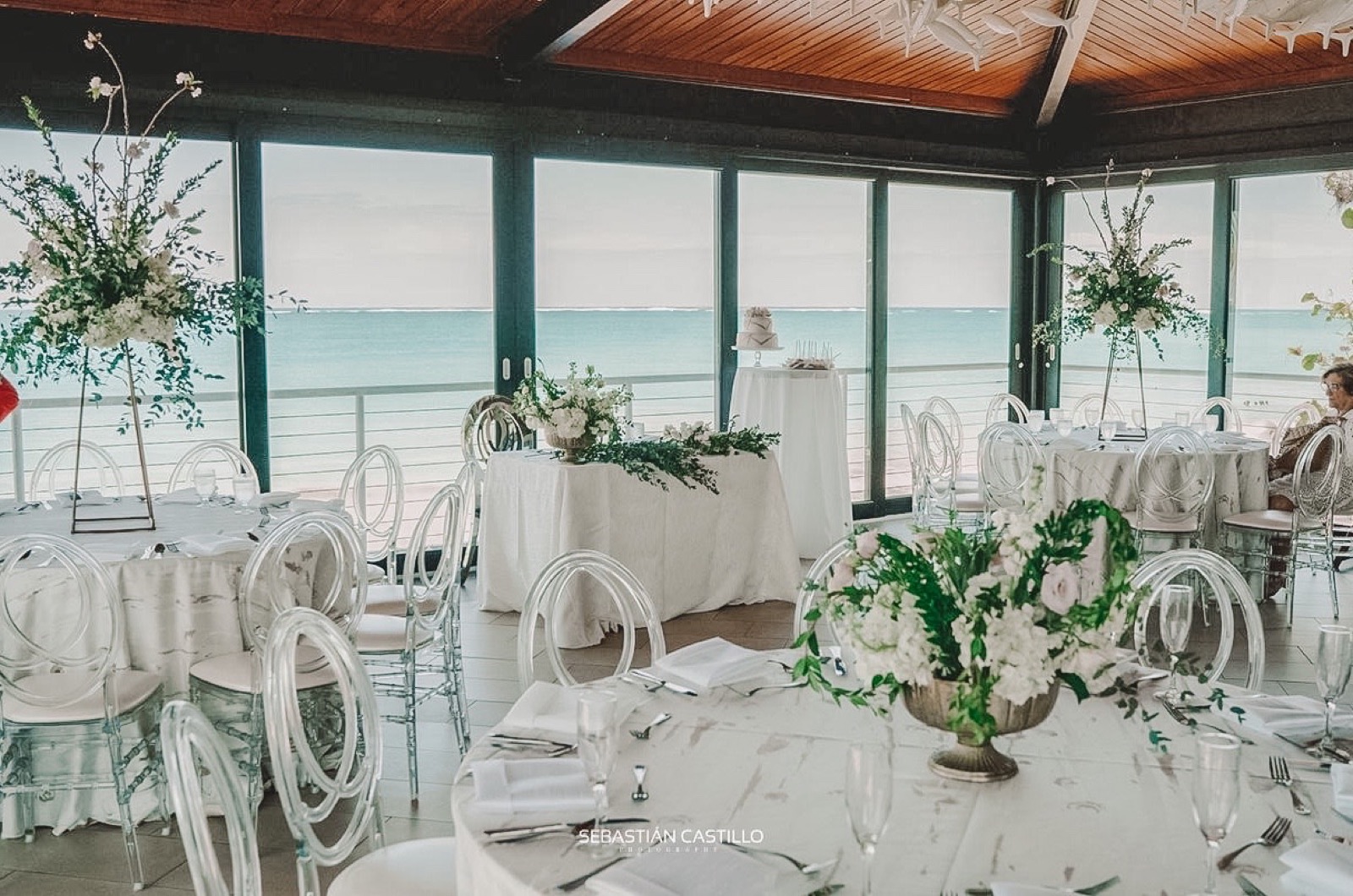 Ocean-view private event dining room with white chairs and floral centerpieces