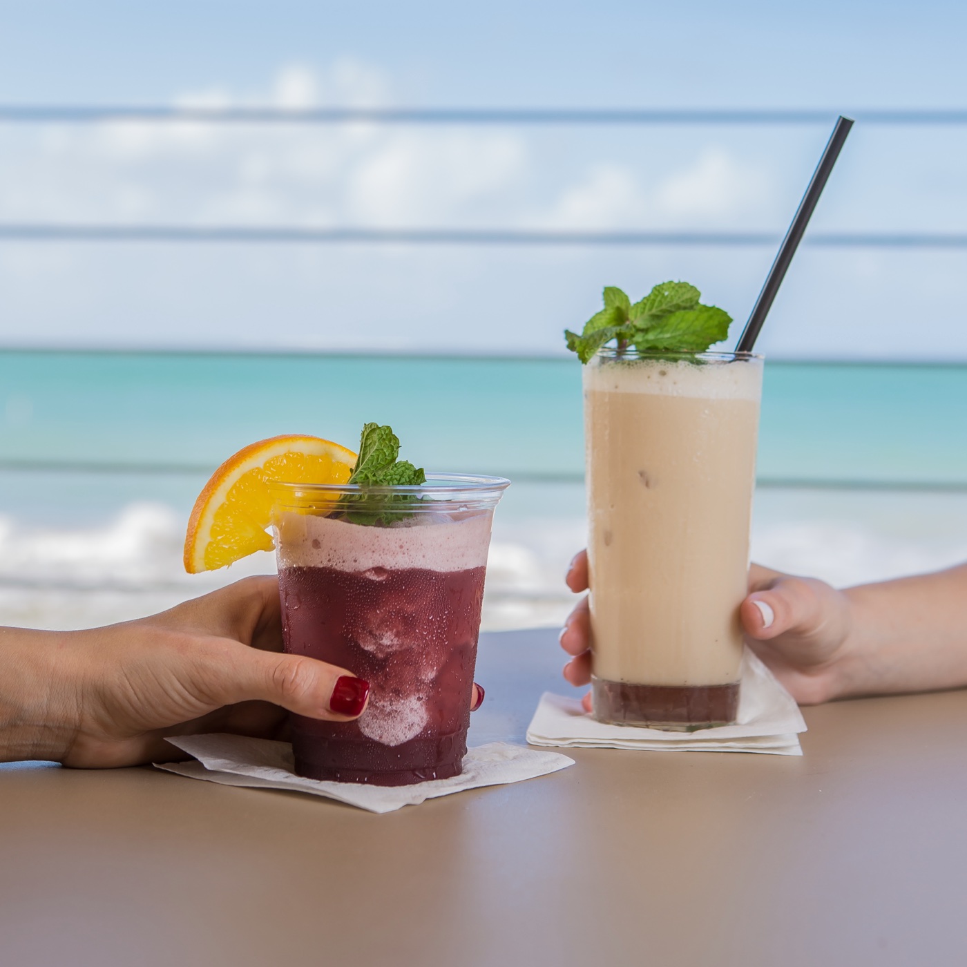 Two tropical drinks held in front of the ocean at Vivo Beach Club